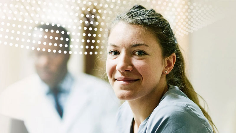 A smiling nurse in medical scrubs with a doctor behind her