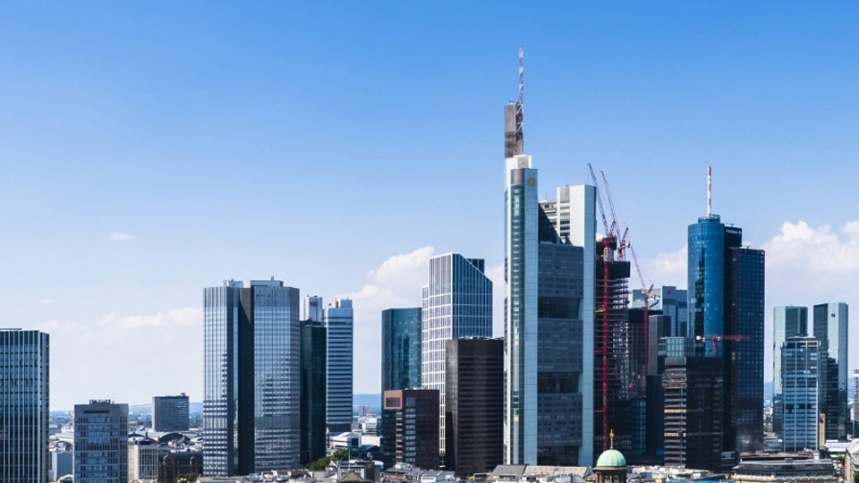 Auf dem Foto ist die Skyline von Frankfurt am Main vor blauem, leicht wolkenbehangenem Himmel zu sehen.