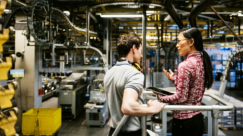 Ein Mann und eine Frau arbeiten an einem Tablet in einer großen Fabrikhalle