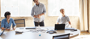 Zwei Männer und eine Frau bei der Teamarbeit - auf dem Tisch stehen mehrere Surface Devices