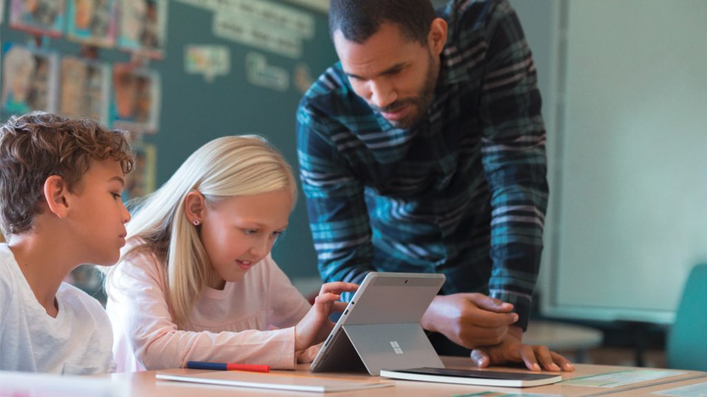 Zwei junge Schüler arbeiten unter Aufsicht eines Lehrers im Klassenzimmer an einem Tablet