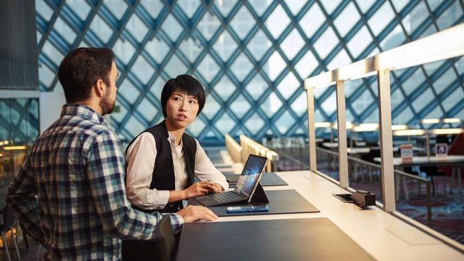 Woman and man sitting at a desk having a conversation in the Seattle Public Library with Surface Pro 4.