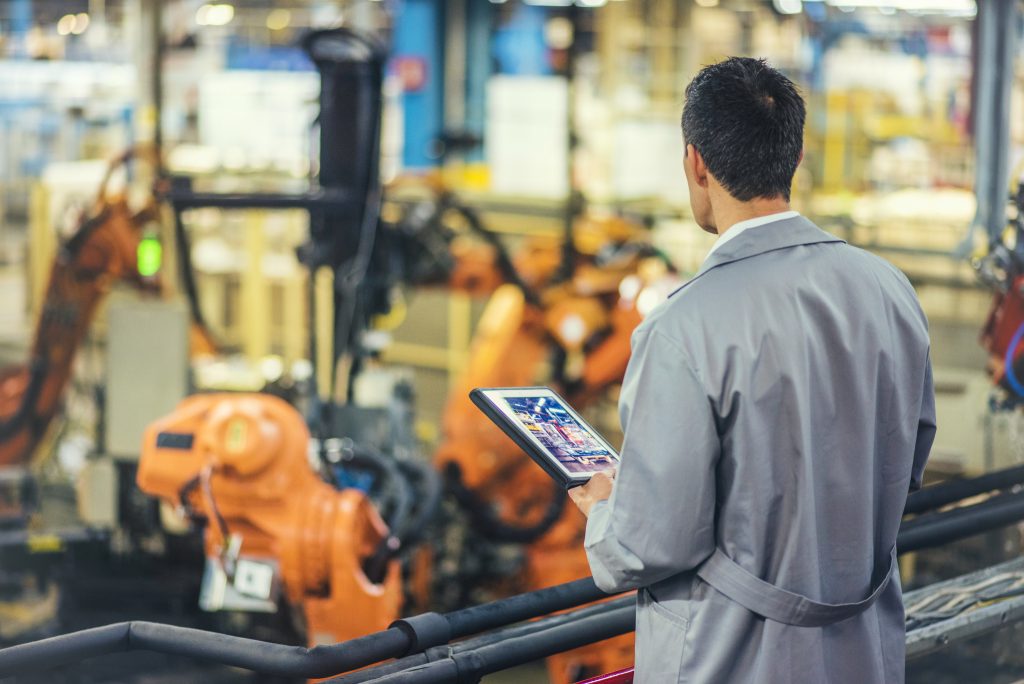 Ein Mechaniker in einer Fabrikhalle hält ein Tablet in der Hand