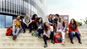 Mehrere Studentinnen und Studenten sitzen auf einer Treppe vor einem Gebäude