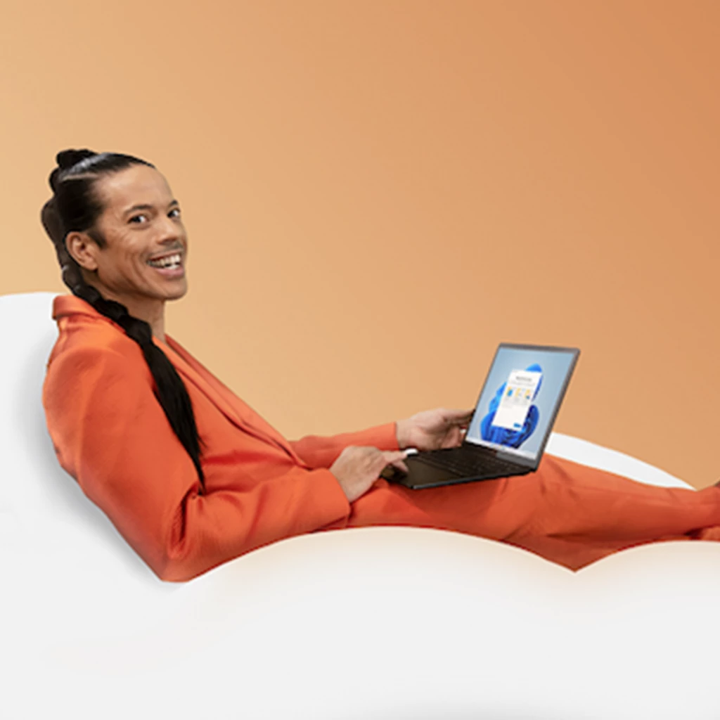 Auf dem Bild ist Jorge Gonzales zu sehen. Dieser sitzt auf einer Woke mit einem Surface auf seinem Schoß. Er lacht strahlend in die Kamera. Er trägt einen orangenen Anzug.