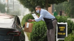 Ein Mitarbeiter eines Restaurants beliefert einen Kunden, der in seinem Auto sitzenbleibt