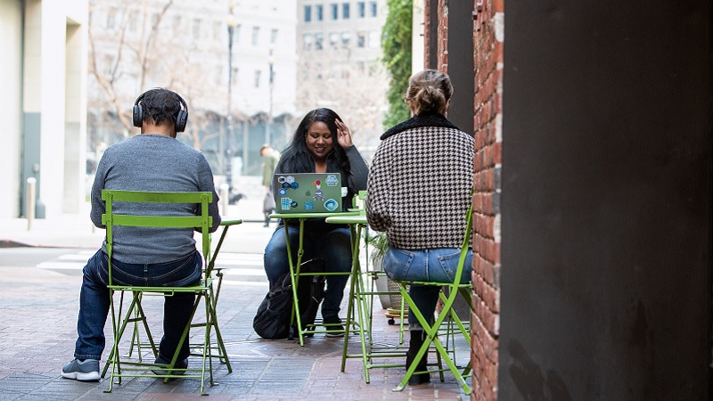 Drei Personen sitzen an Einzeltischen in einem Straßencafé