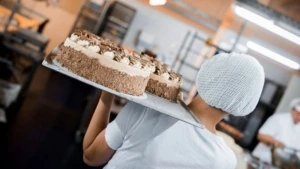 Eine Konditorin, von hinten fotografiert, trägt eine Sahnetorte