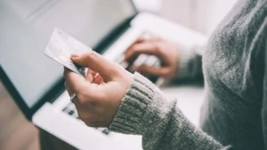Eine Person bedient mit ihrer rechten Hand einen Laptop, während ihre linke eine Bankkarte hält.