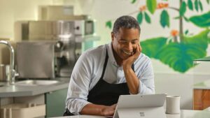 Mann in einer Kochschürze steht in einer Restaurantküche und blickt auf ein Surface Laptop Pro