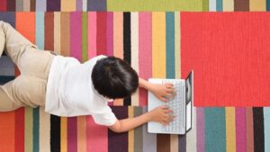 Ein Kind im Grundschulalter liegt zu Hause auf einem Teppich und arbeitet mit einem Surface.