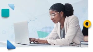 Eine junge Frau mit Brille und weißem Mandel sitzt an einem Laptop.