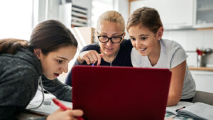 Eine Mutter helft ihren Kindern bei den Hausaufgaben am Laptop.