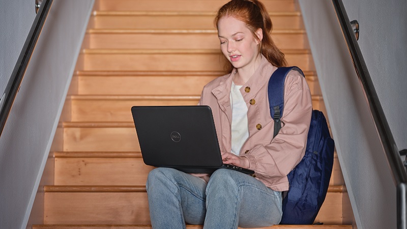 Ein Mädchen sitzt auf einer Treppe, auf ihren Knien hält sie einen Laptop