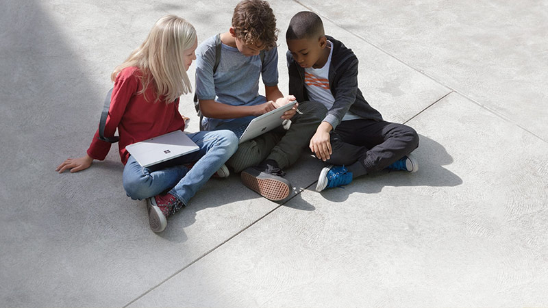 Schulkinder sitzen auf dem Pausenhof und schauen gemeinsam auf ein Tablet