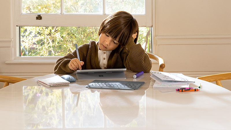 Ein Schulkind sitzt am Küchentisch und macht Hausaufgaben am Touchscreen eines Surface