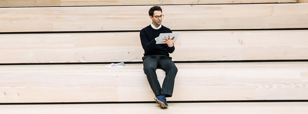 Ein Mann sitzt mit einem Tablet auf hölzernen Stufen.