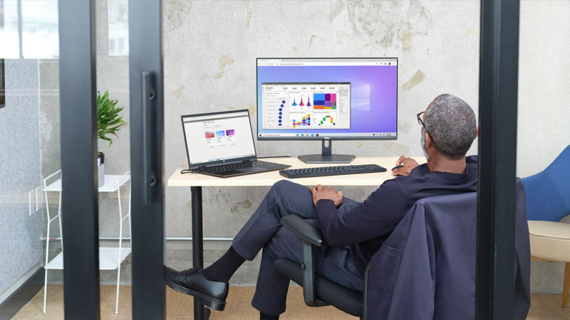 Eine Persaon sitzt vor einem Laptop und einem Bildschirm, auf beiden ist eine Power Bi Anwendung zu sehen.