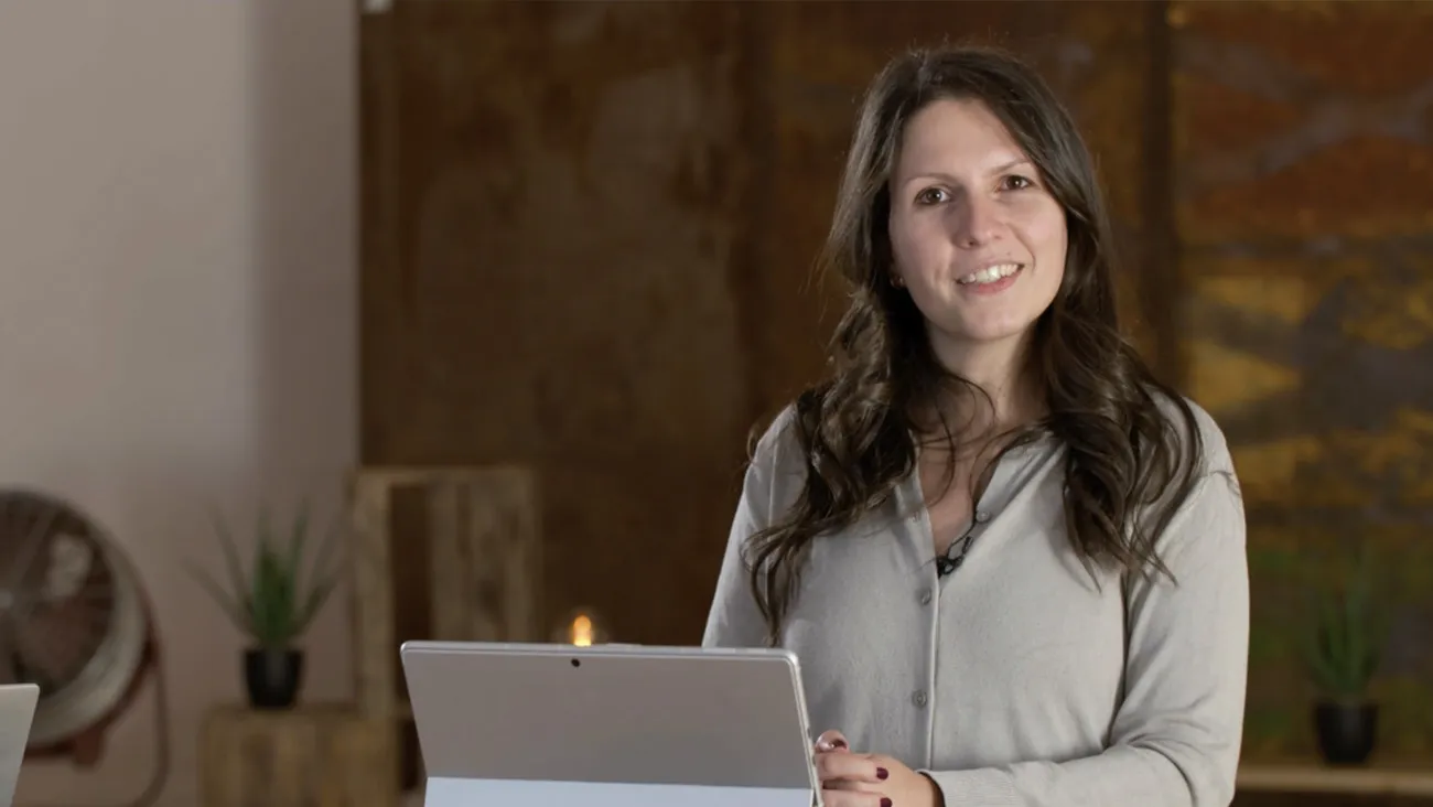 Eine Frau steht als Moderatorin an einem Pult mit einem Laptop.