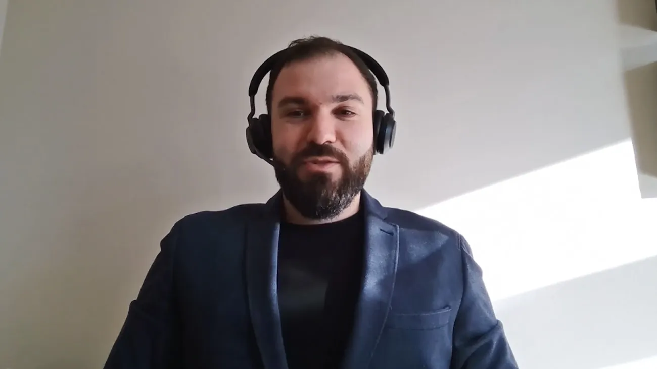 Ein Mann mit Kopfhörern steht als Moderator in einem Büro.