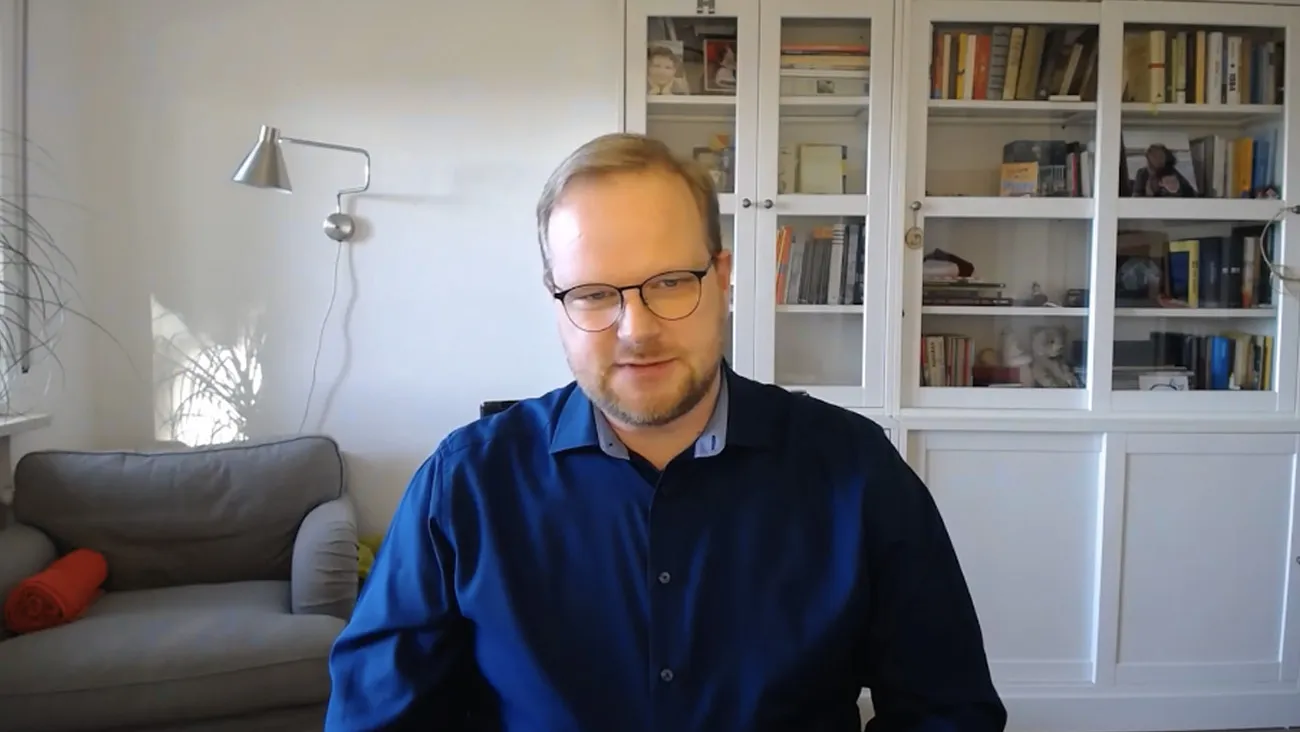 Ein Mann sitzt als Moderator in einem Büro an einem Schreibtisch.