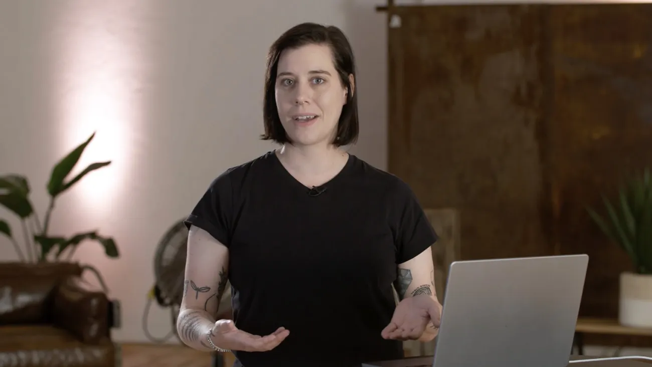 Eine Frau steht als Moderatorin an einem Pult mit einem Laptop.