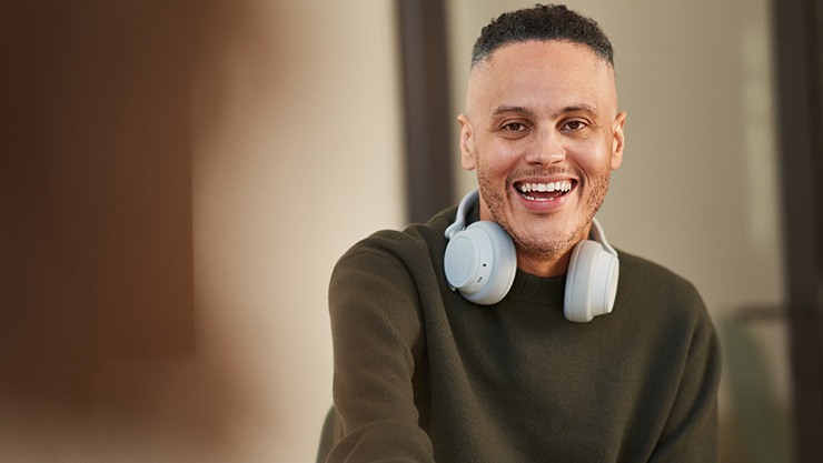 A man with a fade haircut and light headphones around his neck smiles broadly at the camera.