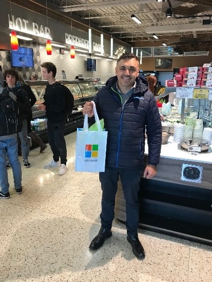 A nominated SMB winner holding a Microsoft bag with giveaway items at his place of business (grocery store)