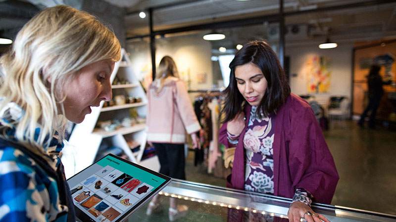 A women uses a surface tablet to help a female customer in a small SMB boutique retail shop.