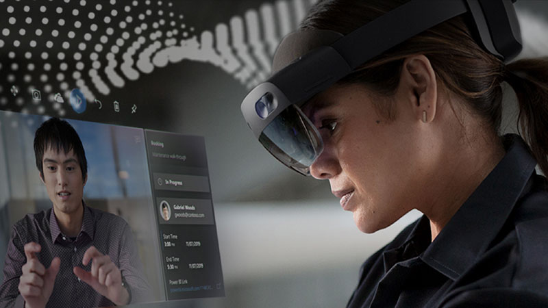 A woman wearing a HoloLens 2 headset receives instruction via her desktop PC