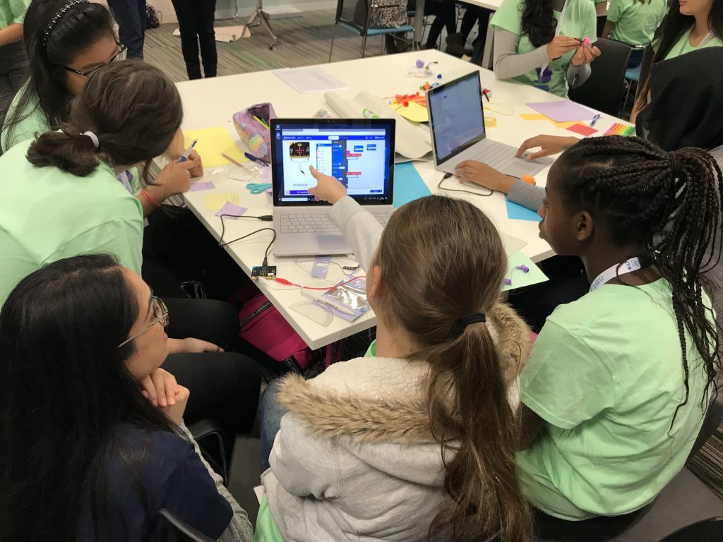 A group of young girls taking part in a Microsoft DigiGirlz event at Microsoft UK. They are all sat at a table looking at content on a Surface