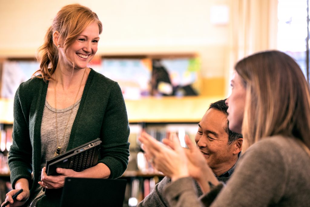 A female teacher leading a discussion with a group of teachers, in a library.