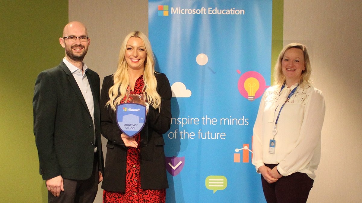 Two women and one man smiling in front of a Microsoft Education banner