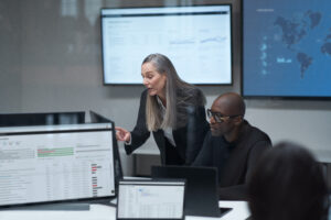A CISO discusses cybersecurity with her colleague in an office with multiple screens