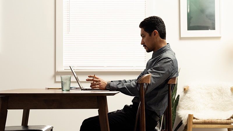 : A male working remotely on his laptop at his dining table