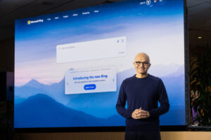 Man smiles as he stands in front of a large screen introducing the new Bing