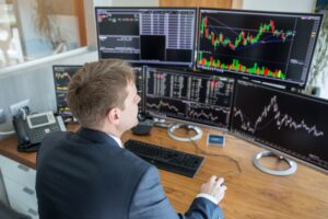 Man in front of three monitors showing charts denoting trading activity.