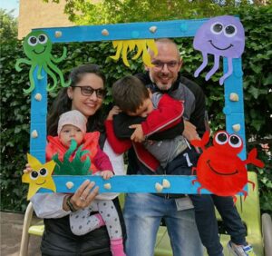 Mother, father and their two children pose behind a colorful frame decorated with sea life and a star.