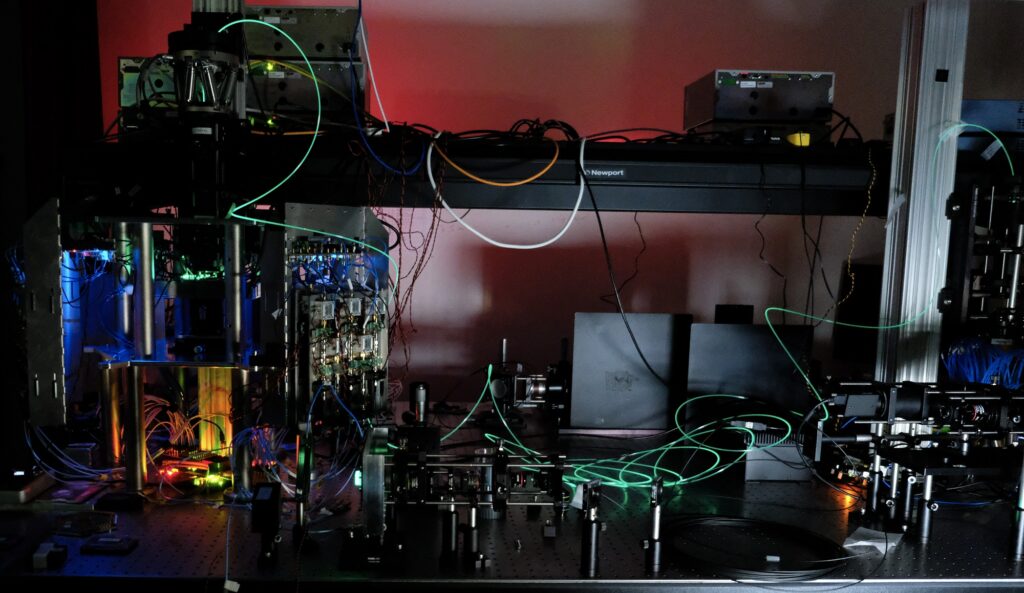 On a metallic table with vertical metal supports, glowing cables and lights illuminate a complicated array of machinery.