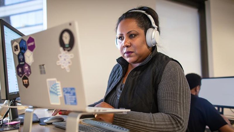 A woman seated at a desk, working on two monitors with a keyboard in front of her.
