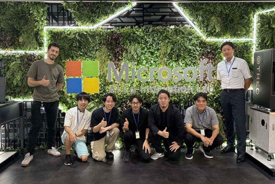 A group of seven men poses in front of a green, plant-covered wall featuring the Microsoft logo and 'AI Co-Innovation Lab' signage.