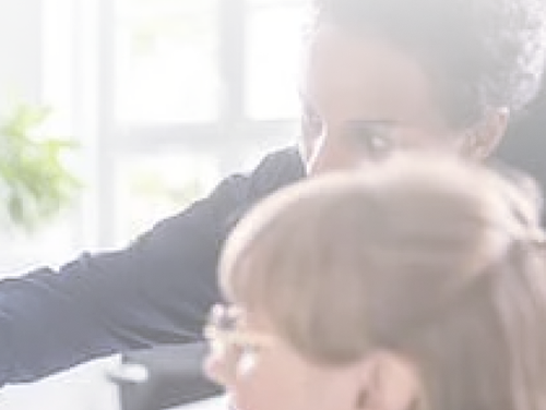 Two women in an office, one gesturing with her arm while talking to the other.