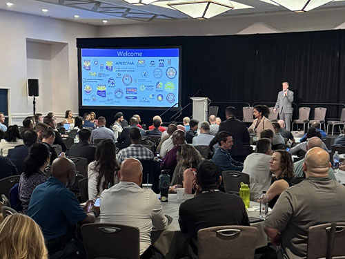A large group of people seated at tables in a conference room, engaged in discussion and collaboration.