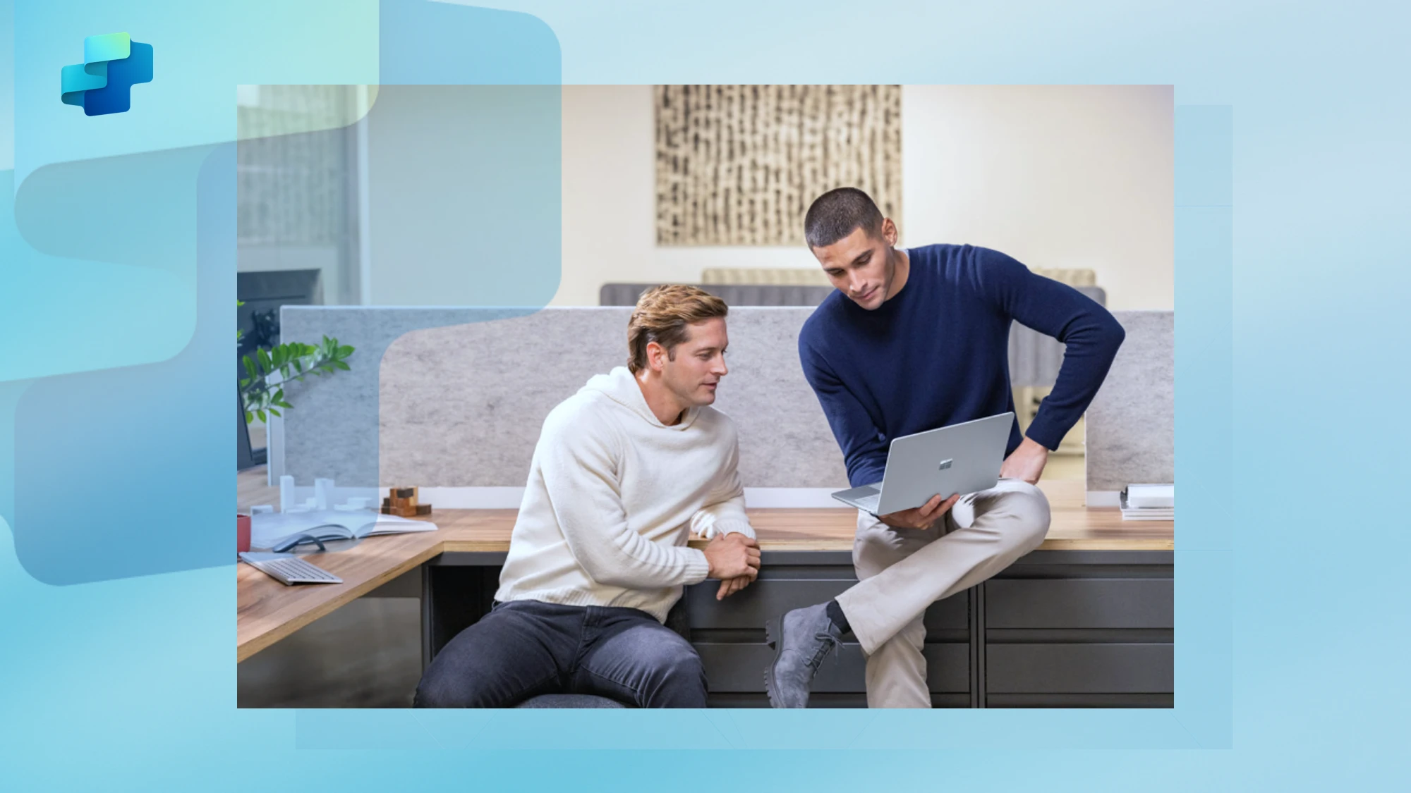 A man sitting on a desk showing another person a laptop screen