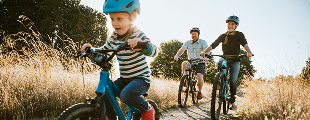 One child riding a bicycle along a grassy trail, with two parents cycling behind.