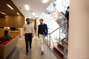 Two people walking down a bright hallway.