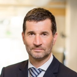 a man wearing a suit and tie smiling and looking at the camera