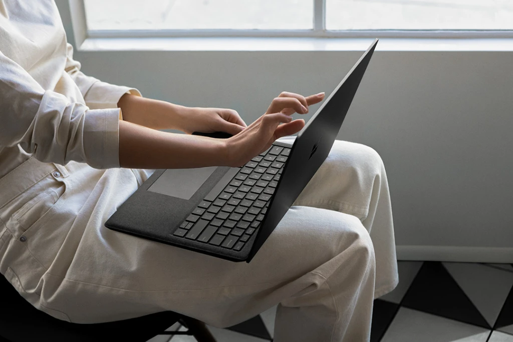 Contextual image of woman touching screen while working on Black Surface Laptop 2