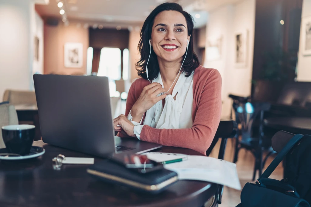 aAwoman sitting at a table with a laptop and smiling at the camera