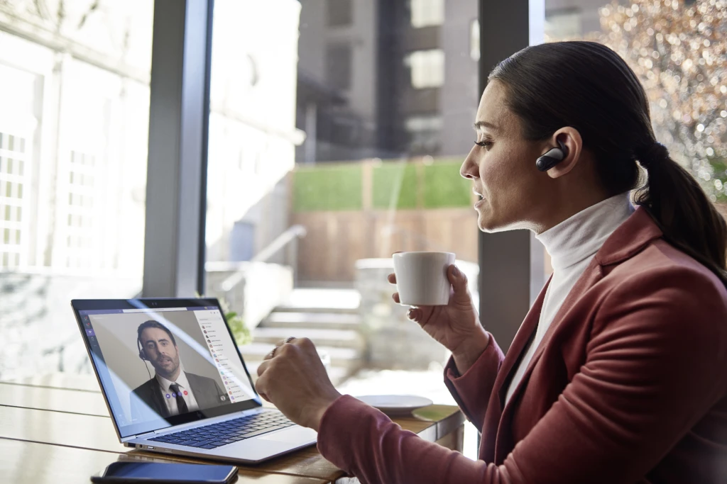 Female small business executive using HP Elite device running Microsoft Teams conference call. Different screens are available: one featuring 1 person on screen, another with 9 people on screen. Keywords: Microsoft Teams, Bluetooth, coffee.